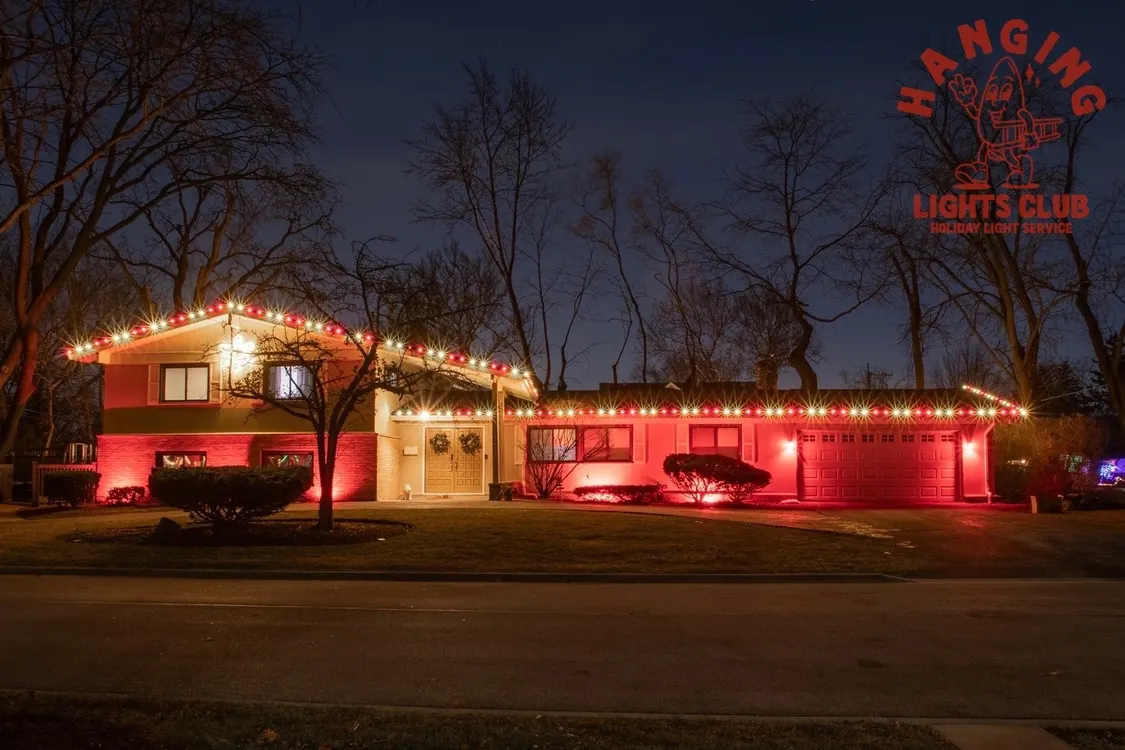 Suburban house with red and warm white holiday lights on the roofline and red uplighting on the bushes