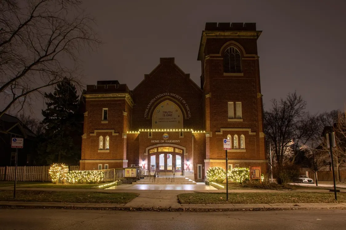 Historic brick church building in Chicago decorated with warm white Christmas lights outlining the entrance and railings at night