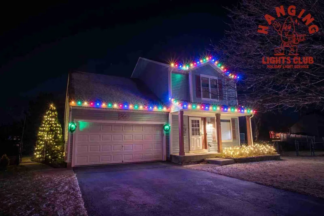 House with colorful Christmas lights along the roofline and lit trees