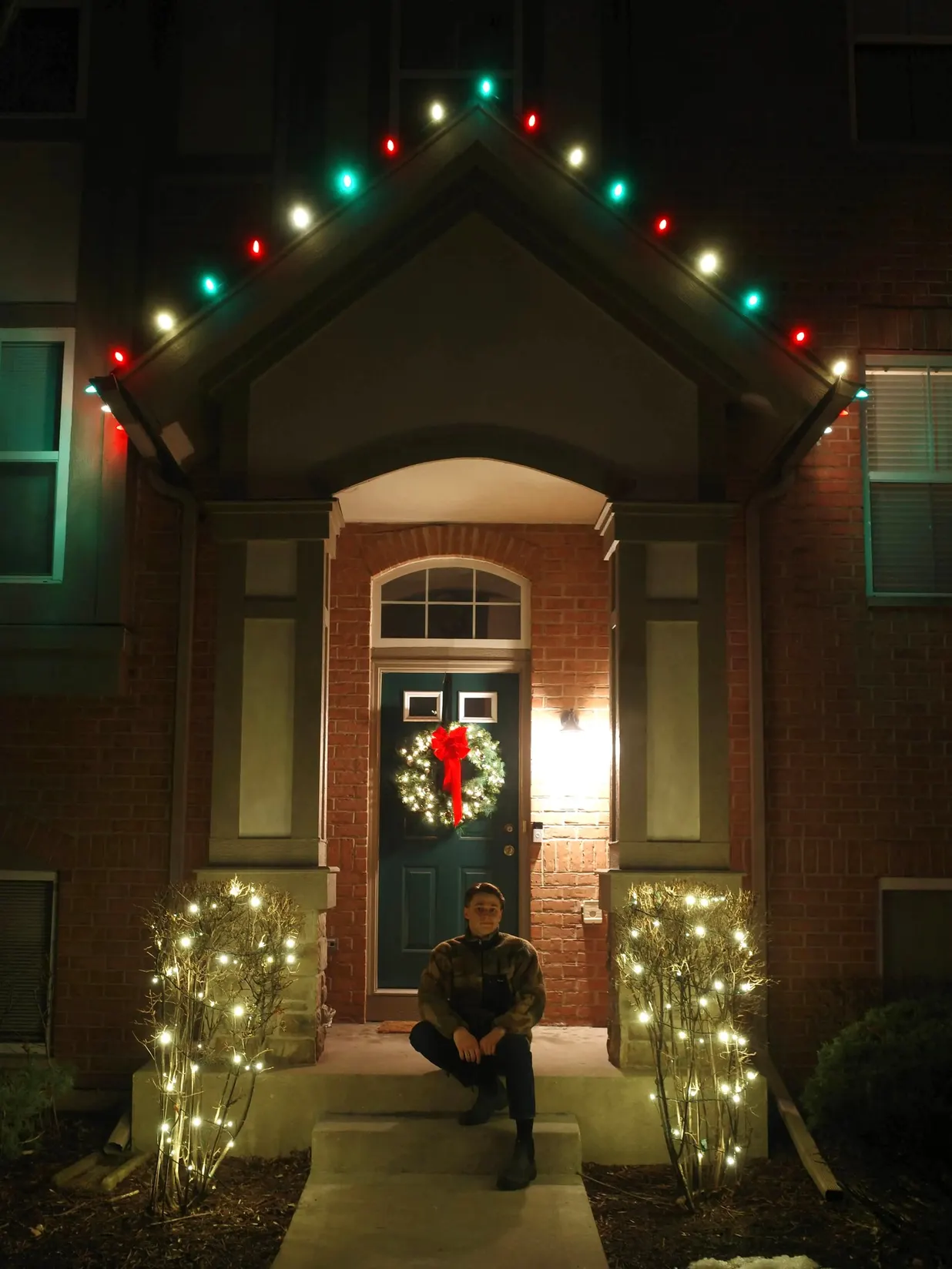 Vitalii, the founder, sitting on the steps of a beautifully lit home with holiday lights