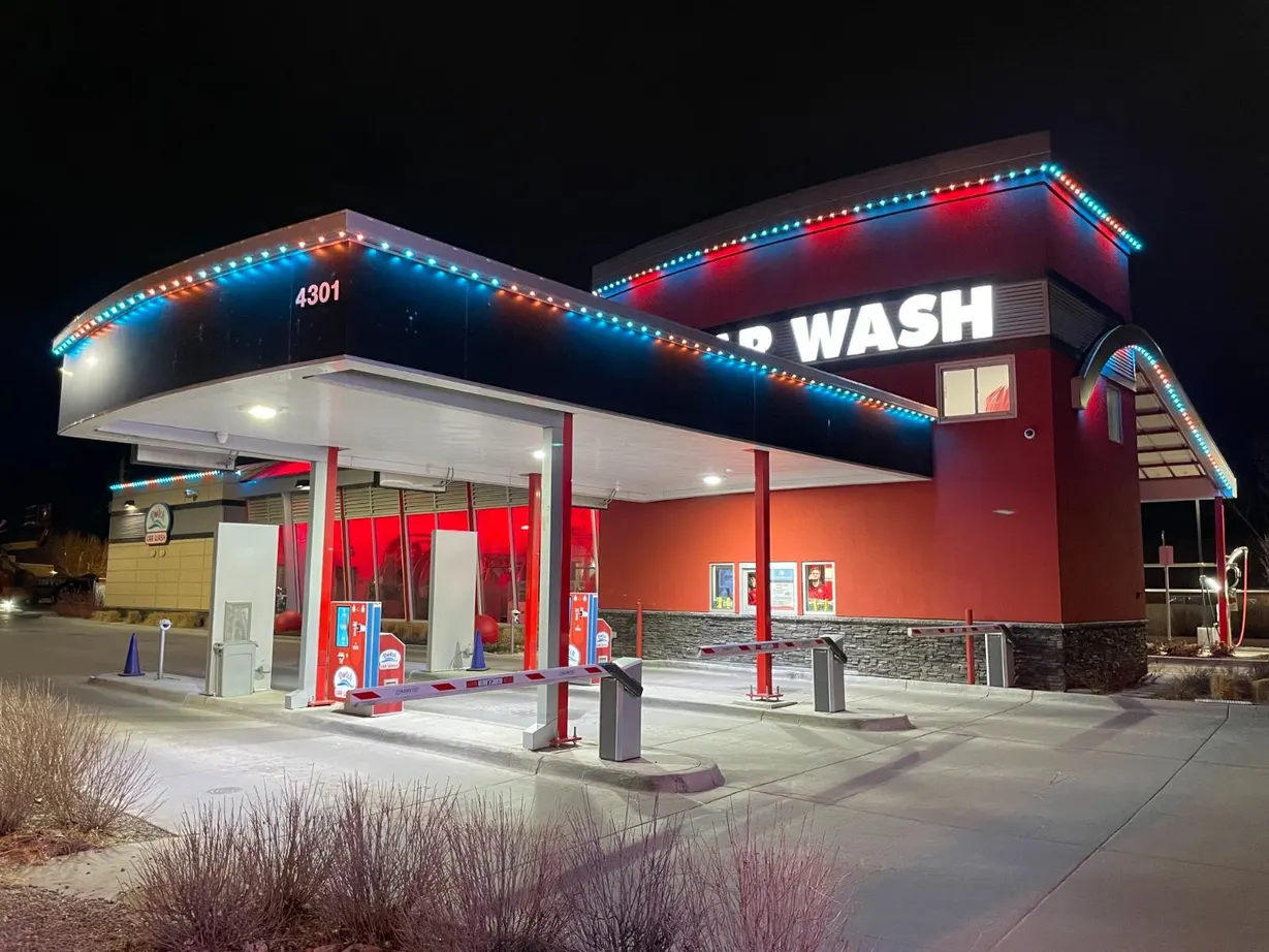Professional car wash building at night with vibrant blue and red LED lighting around the roofline and signage
