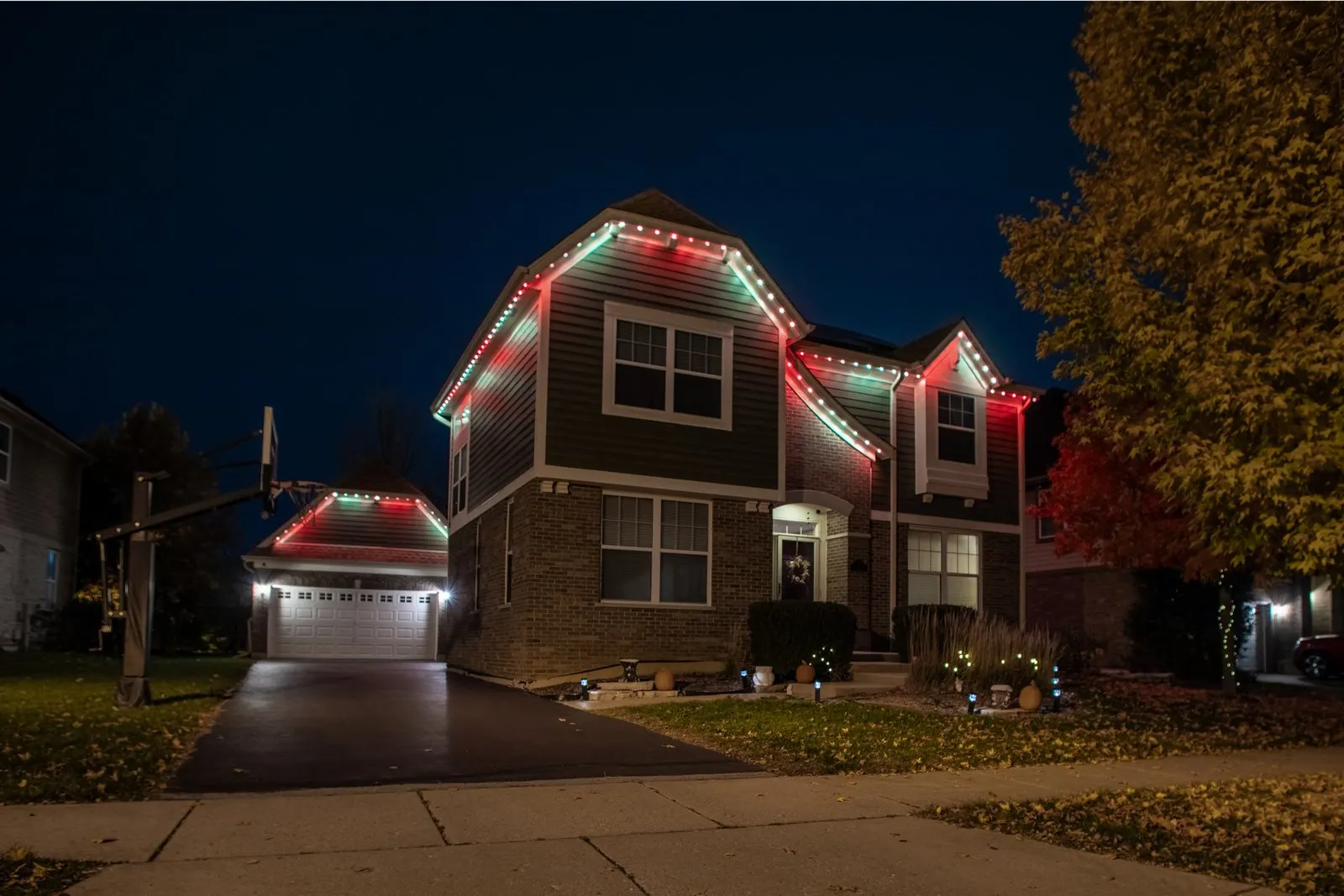 Two-story brick house illuminated with professional red and green permanent RGB LED lights along the roofline