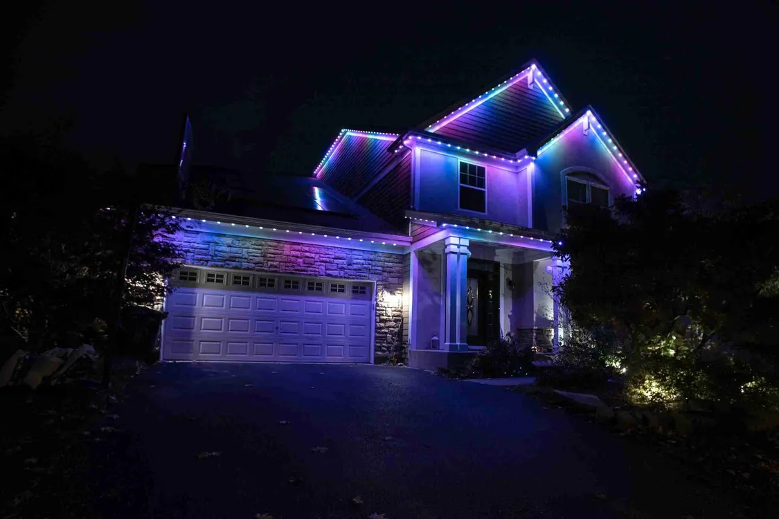 Modern two-story house at night with vibrant purple, blue, and cyan RGB LED lights outlining the roofline, garage, and architectural features