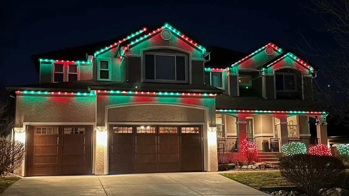 Residential home with red and green permanent holiday lights on the roofline and gables